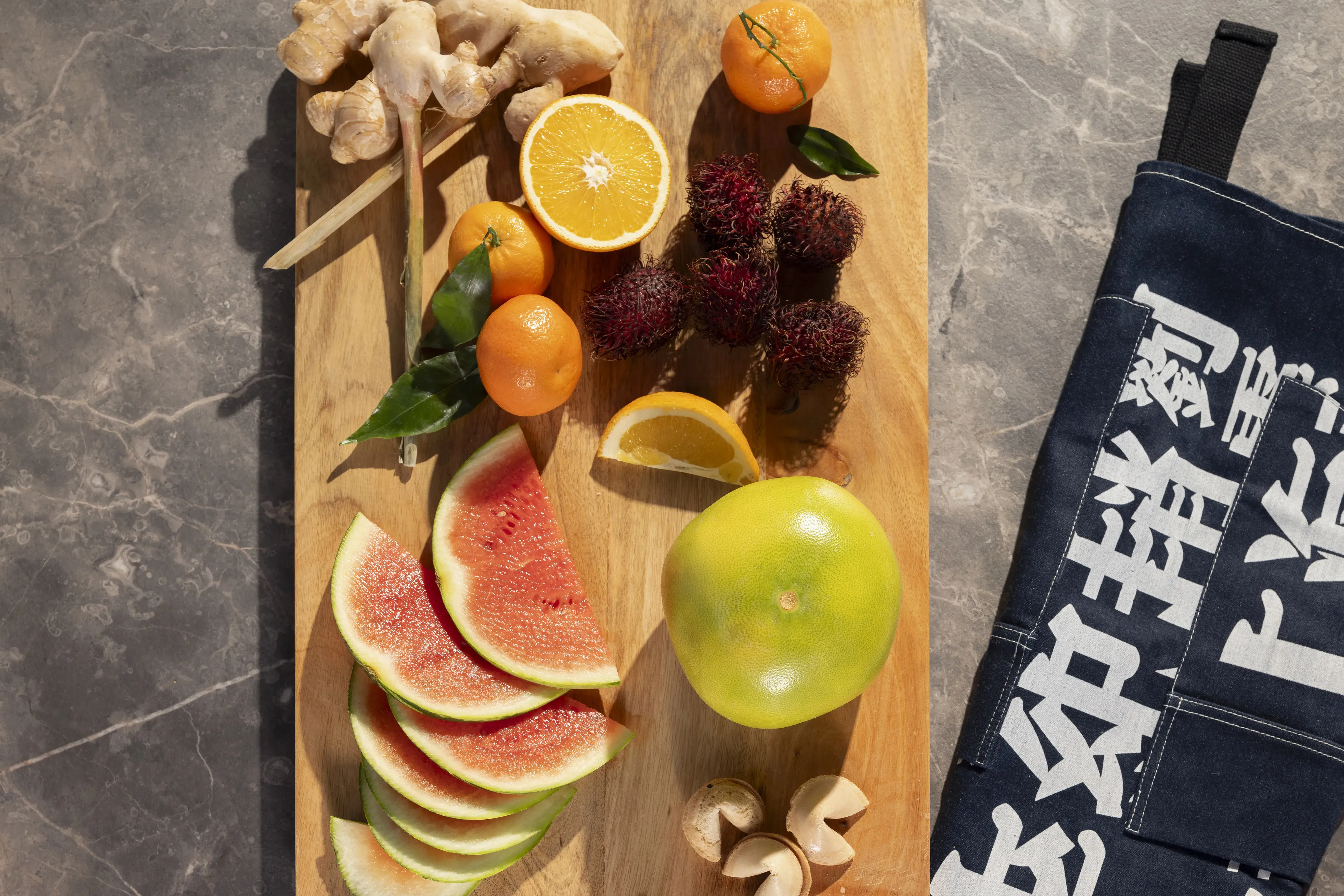 Obst, Ingwer und Pilze auf einem Holzbrett, daneben eine schwarze Küchenschürze