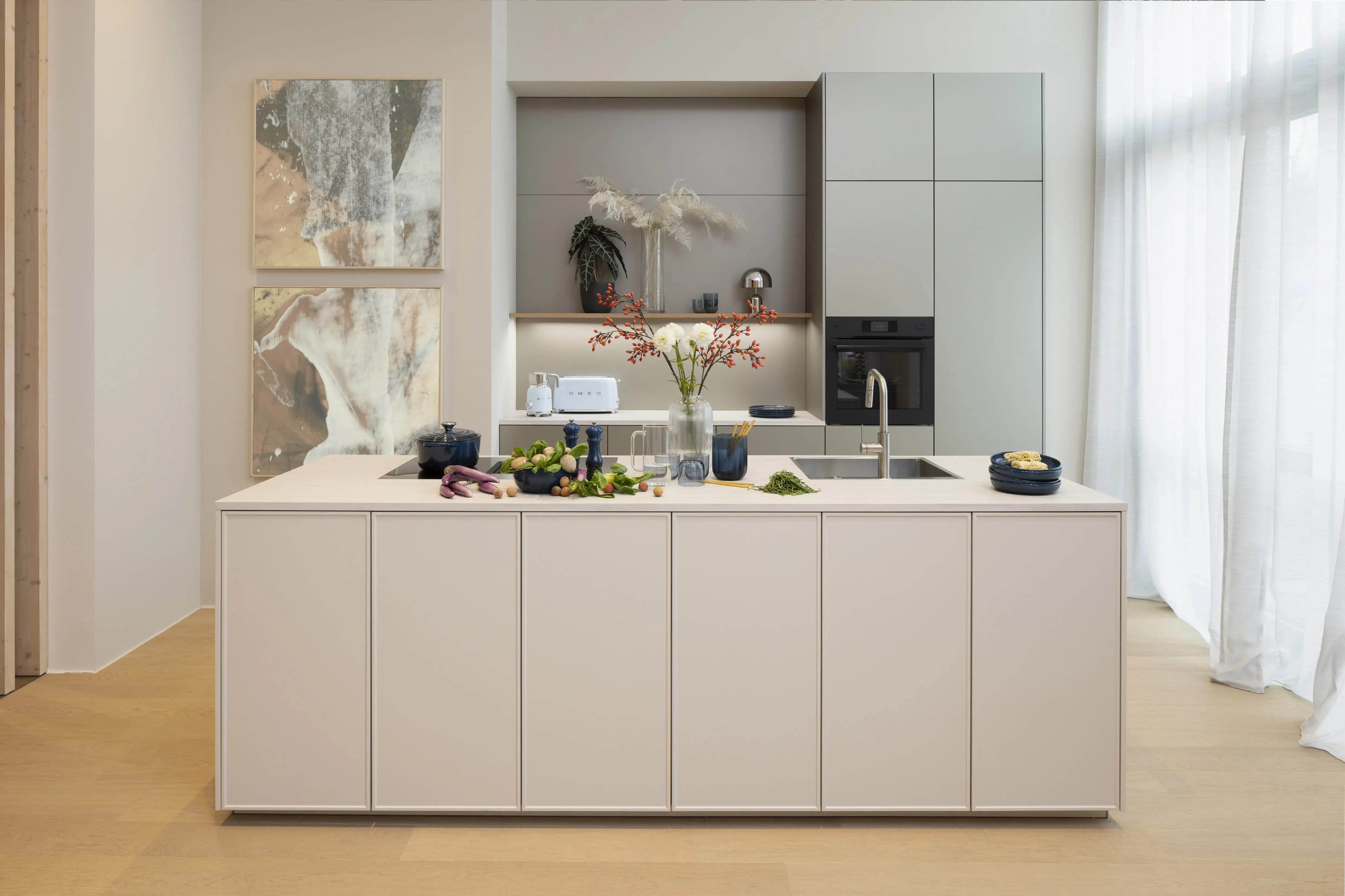 Moderne, helle Küche mit Kochinsel, frischen Zutaten und Blumen in einer Vase.