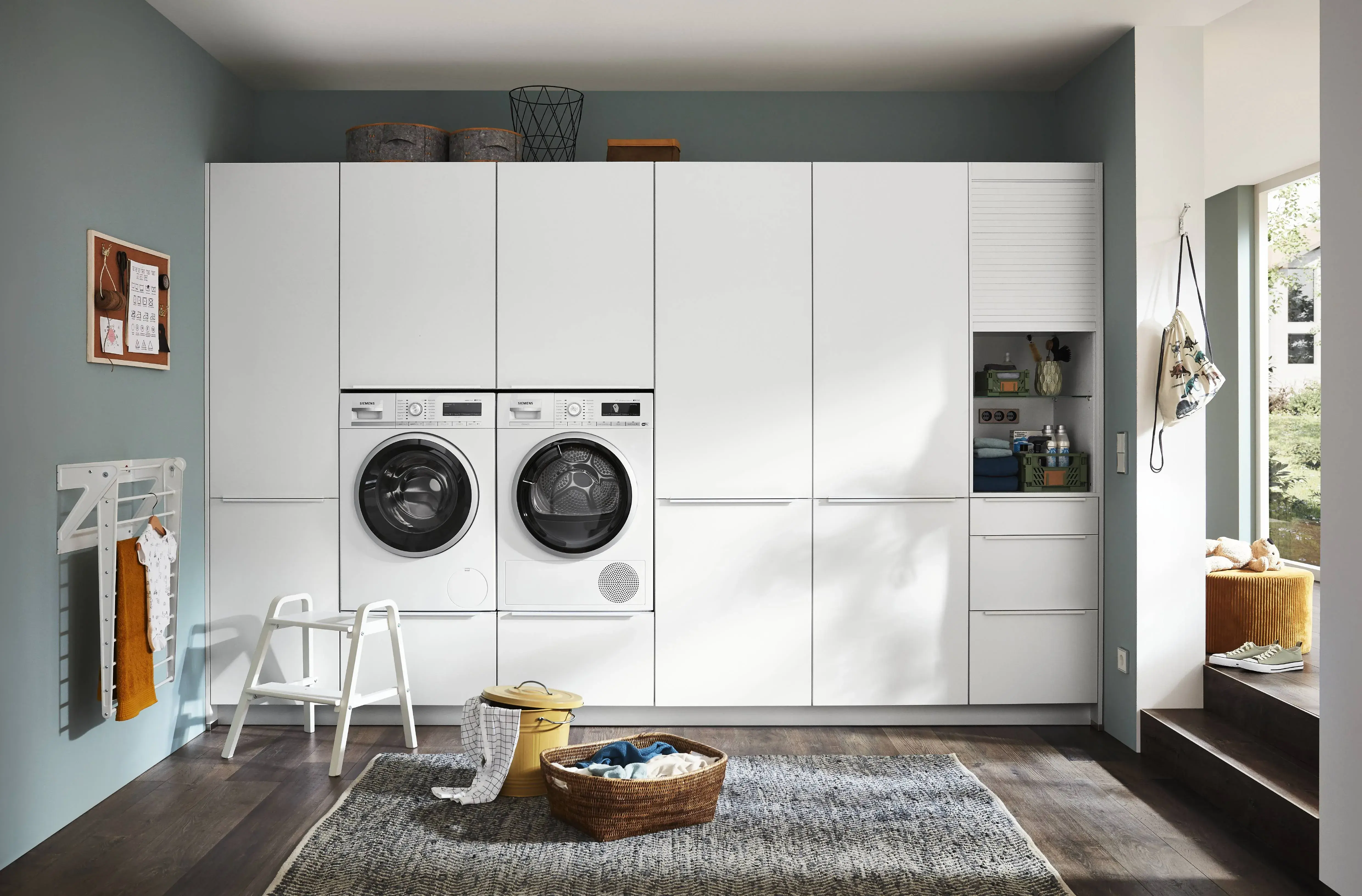 Weisse Schrankwand mit integrierter Waschmaschine und integriertem Trockner nebeneinander in Nobilia Hauswirtschaftraum links an der Wand hängend montierter Wäscheständer