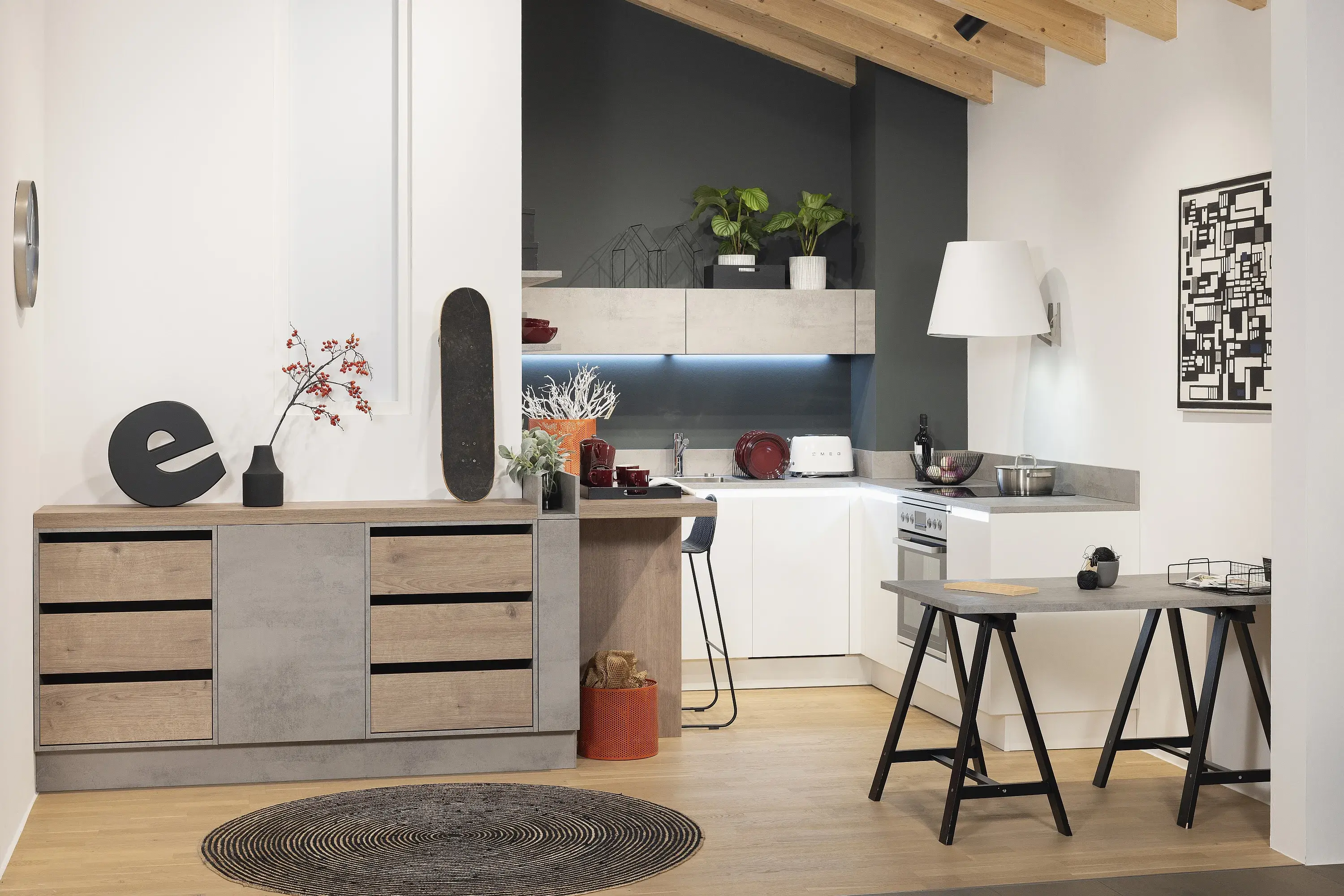 Im Vordergrund Sideboard mit englischen Zügen im Hintergrund in einer Nische kleine weiße Küche mit Esstheke in Holz unter hoher Dachschräge