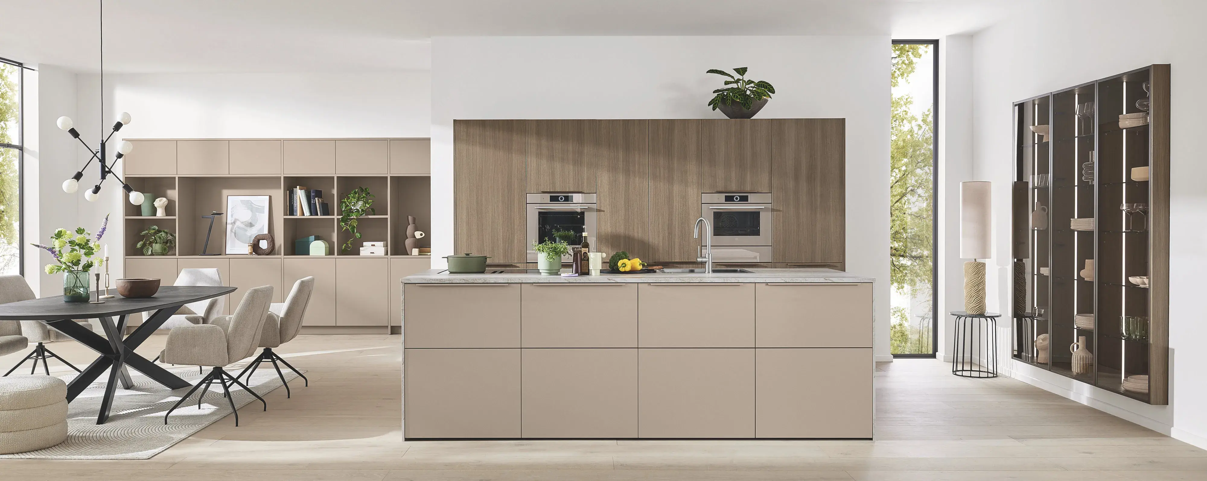 Ballerina offene Inselküche mit Gerätehochschrank dahinter Esstisch links und bequeme Essstühle rechts Einbau-Vitrine mit braun getöntem Glas